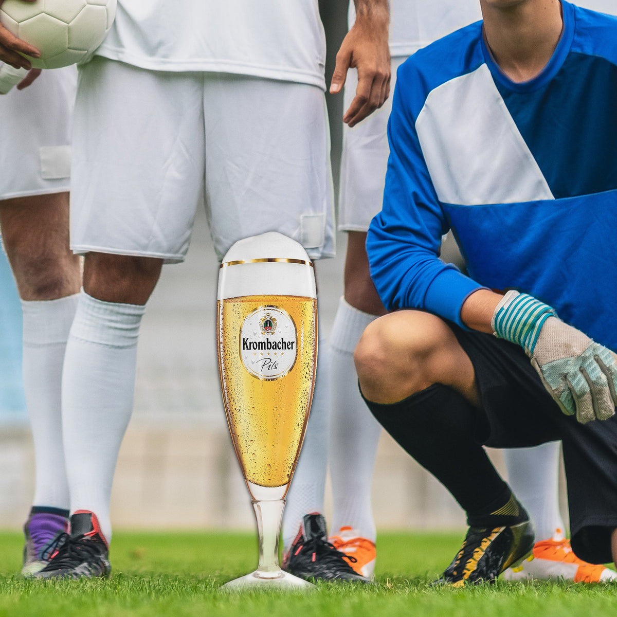 Krombacher Pils Exklusiv Pokal vor Fußballspielern auf dem Fußballplatz.