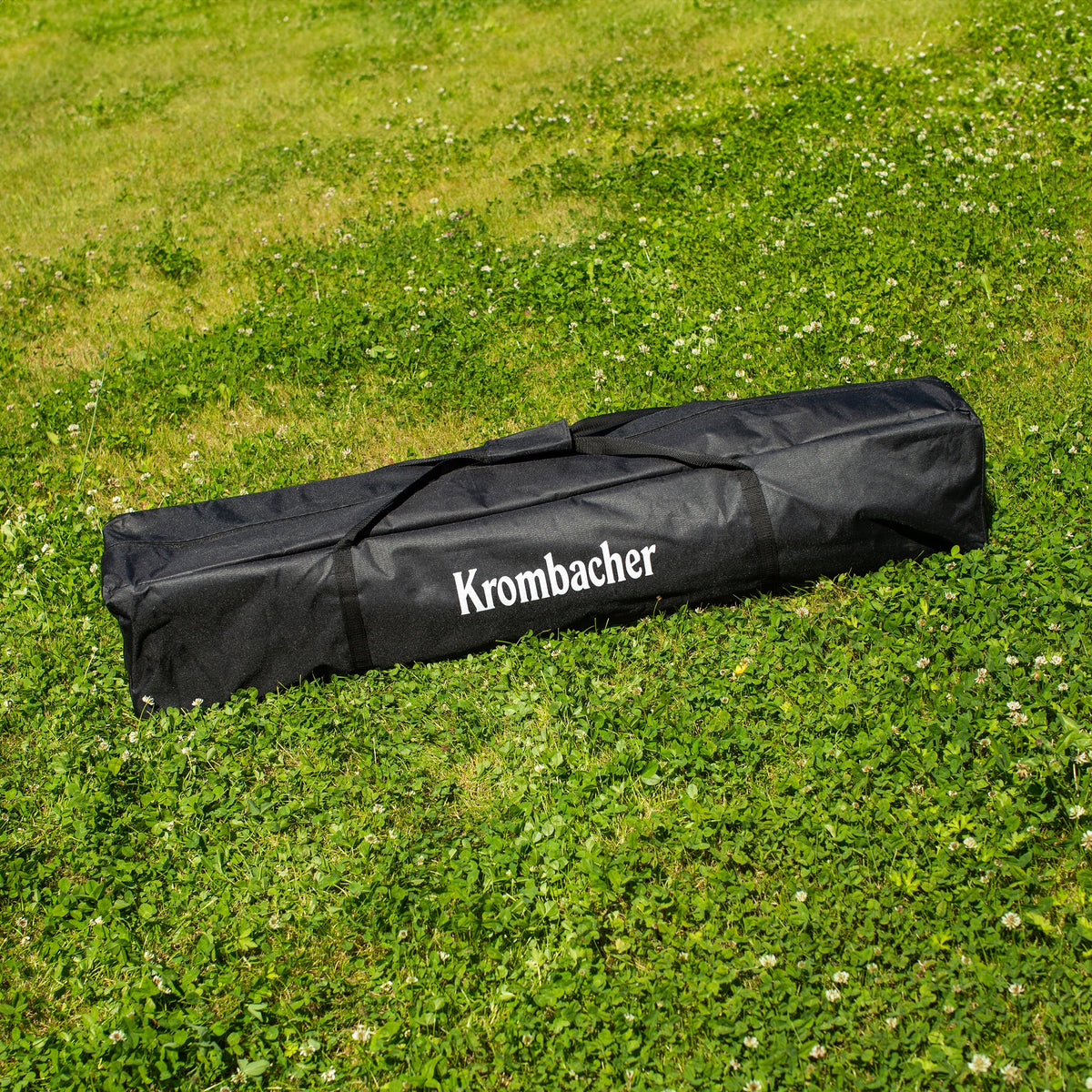Schwarze Tragetasche mit dem Schriftzug 'Krombacher' liegt auf grünem Gras.