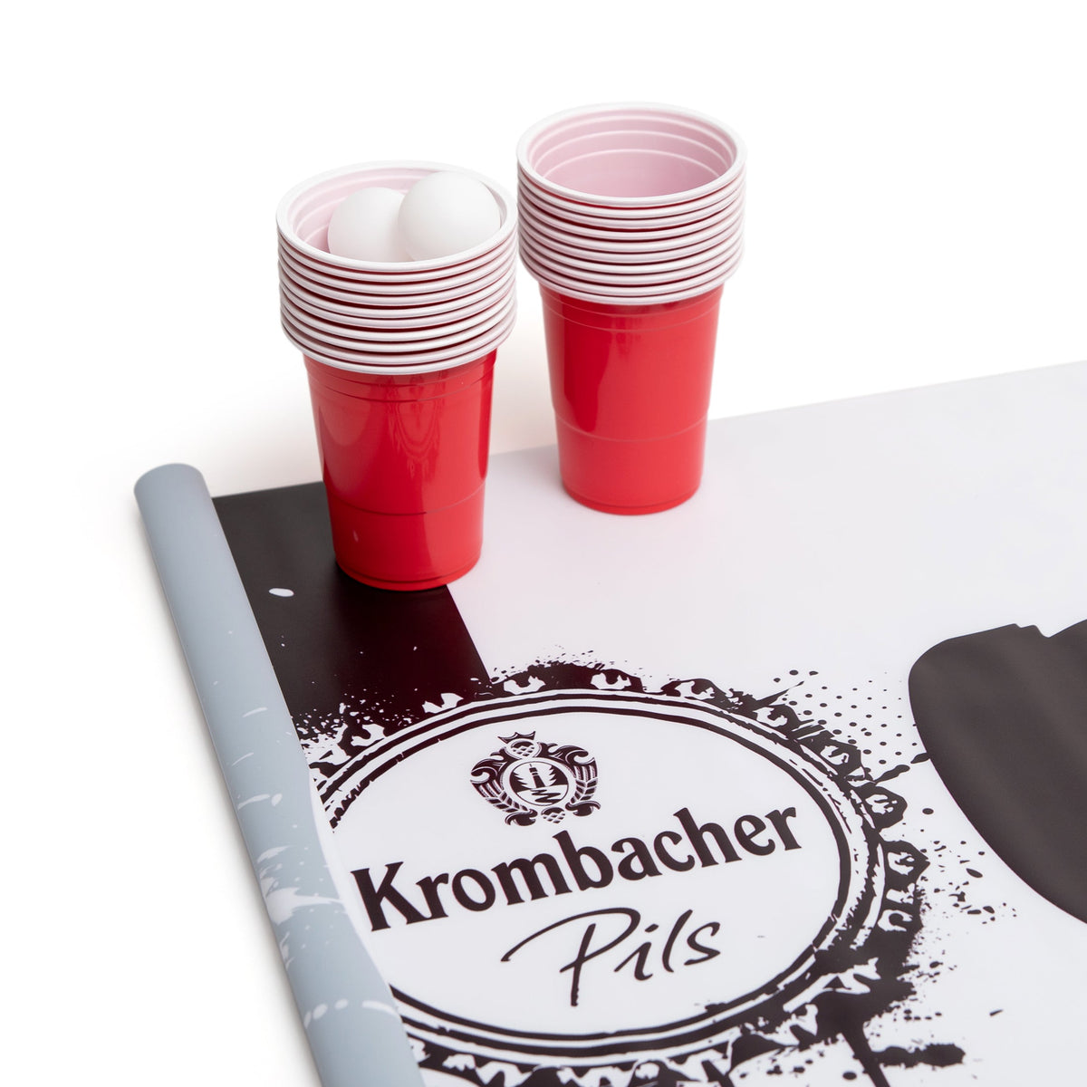 Frau wirft Ball auf rote Becher bei Beerpong-Spiel im Freien, Krombacher Bierflaschen auf Tisch.
