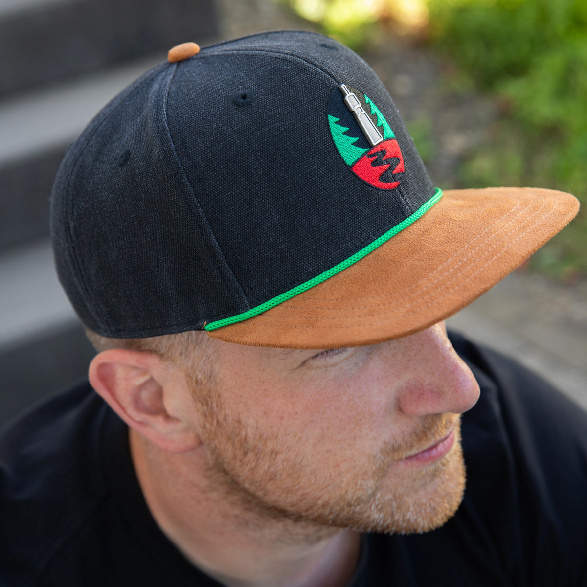 Krombacher Snapback mit braunem Schild und grünem Akzent.