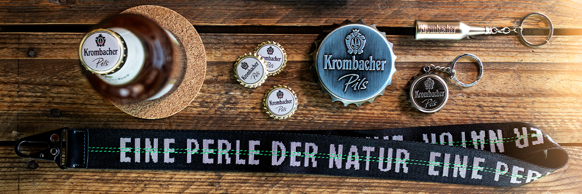 Krombacher Pils Bierflasche, Kronkorken, Flaschenöffner und Schlüsselanhänger mit Krombacher-Logo, Text auf Band: 'EINE PERLE DER NATUR'