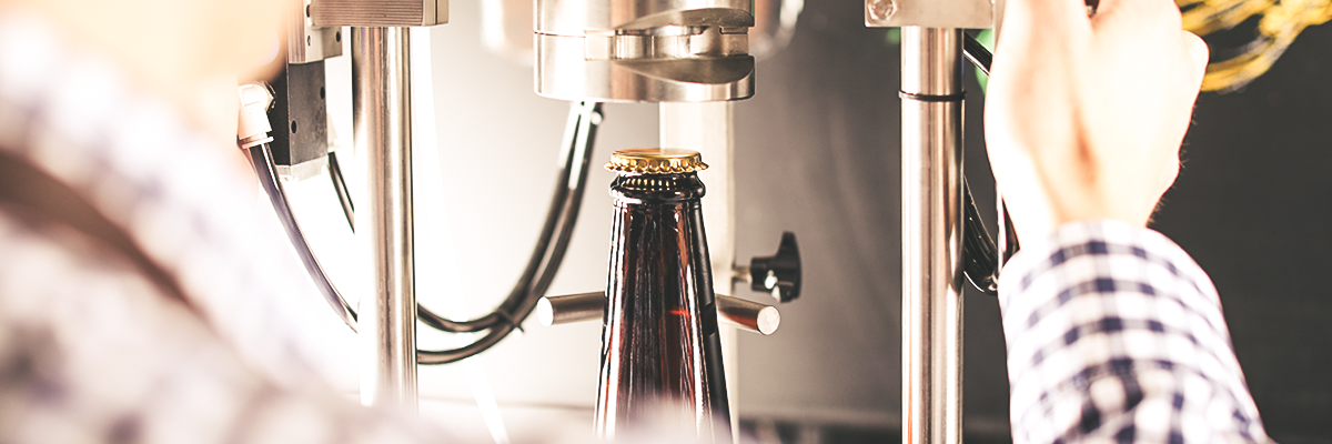 Hand bedient Abfüllmaschine, die eine braune Krombacher Pils 3,0l Flasche mit Kronkorken in einer Brauerei abfüllt