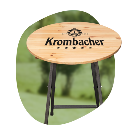 Stehtisch mit rundem Holzplatte und schwarzem Metallgestell, Platte mit Schriftzug 'Krombacher' und Logo.