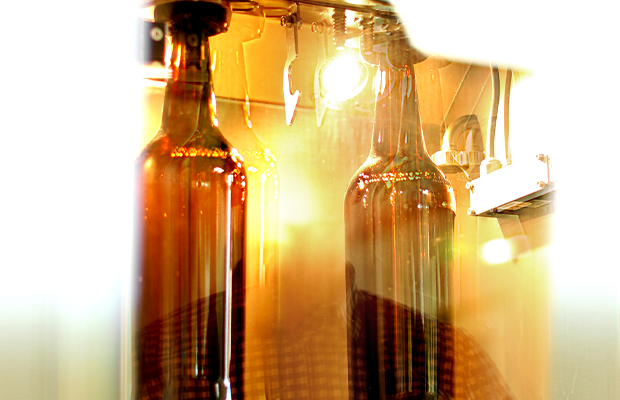 Zwei Krombacher Pils 3,0l Glasflaschen werden in einer Abfüllanlage mit Flüssigkeit befüllt.