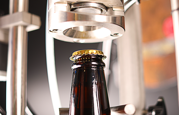 Braune Krombacher Pils 3,0l Flasche mit goldfarbenem Kronkorken unter einer Verschließmaschine