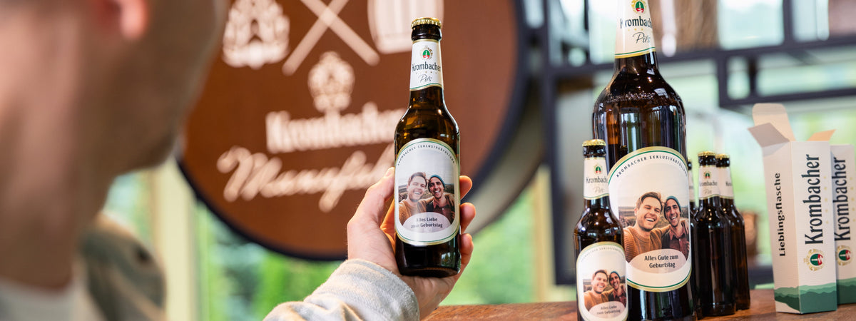 Person hält eine personalisierte Krombacher Pils-Flasche in der Krombacher Manufaktur.