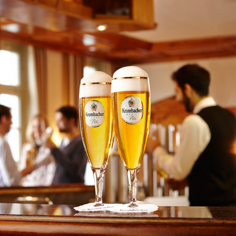 Barszenerie mit zwei frisch gezapften Krombacher Pils in Exklusiv-Pokalgläsern.