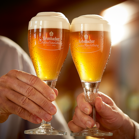Zwei Hände stoßen mit Krombacher Traditionspokalen an.