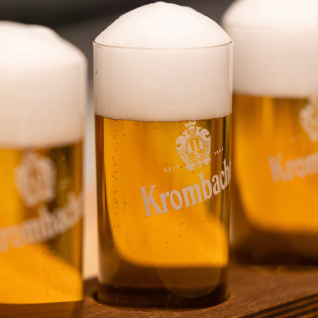 Drei Krombacher Probiergläser gefüllt mit Pils, auf Holzunterlage.