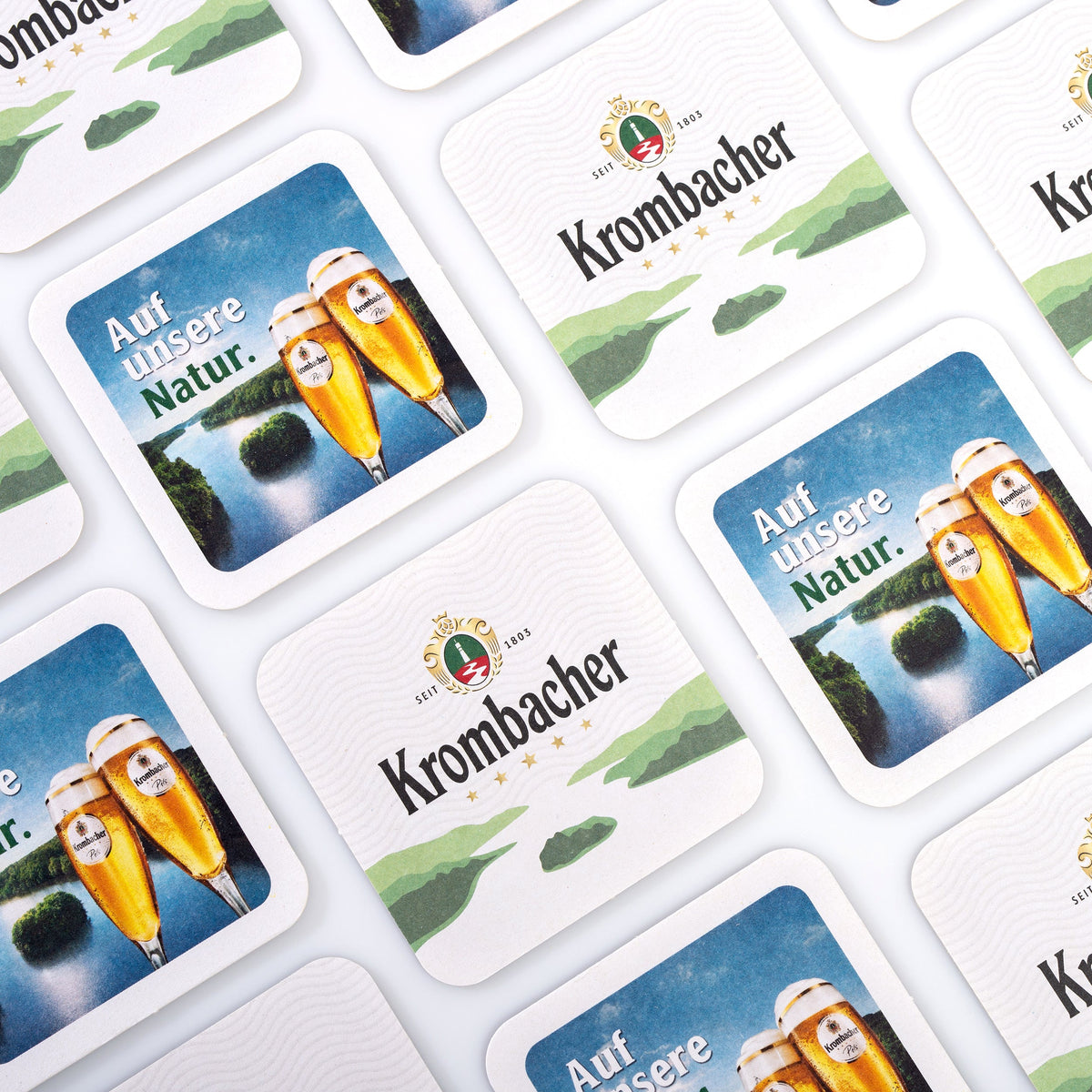 Mehrere Krombacher Bierdeckel mit abwechselnd Vorder- und Rückseite.