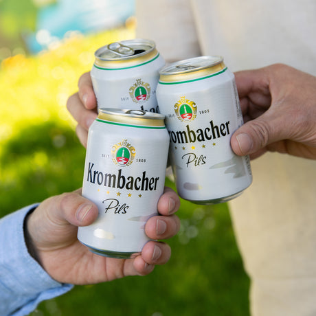 Drei Personen stoßen mit Krombacher 0,33l Dosen in der Natur an.