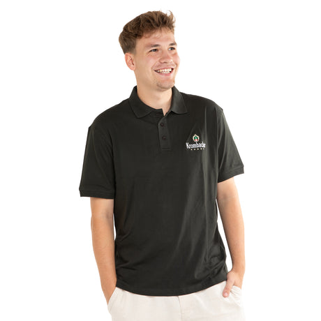Junger Mann trägt dunkelgrünes Poloshirt mit Krombacher-Logo und hat die Hände in den Hosentaschen
