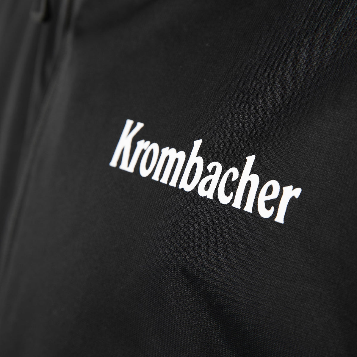 Schwarze Regenjacke mit weißem Schriftzug 'Krombacher' auf der Brust.