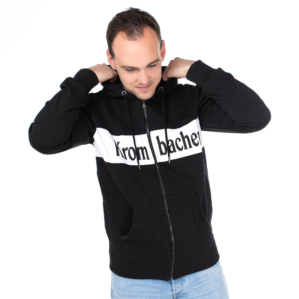 Person trägt schwarze Sweatshirtjacke mit weißem Streifen und Schriftzug 'Krombacher' auf der Brust, hellblaue Jeans.