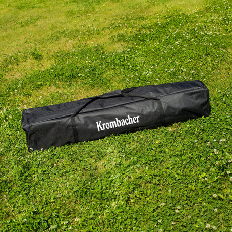 Schwarze Tragetasche mit dem Schriftzug 'Krombacher' liegt auf grünem Gras.