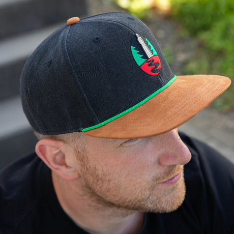 Krombacher Snapback mit braunem Schild und grünem Akzent.