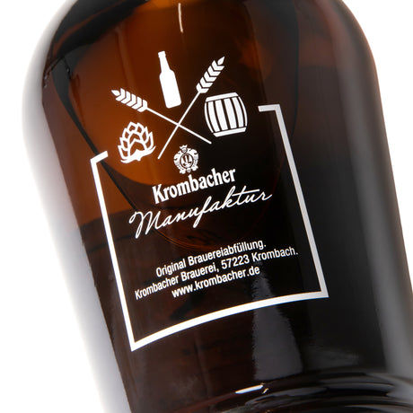 Braune Flasche mit weißem Aufdruck, der Symbole wie Flasche, Hopfen, Gerstenähren und Fass zeigt sowie den Schriftzug 'Krombacher Manufaktur' und weitere Brauereiinformationen