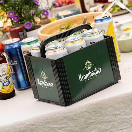 Sechserträger mit Krombacher-Dosen auf einem gedeckten Tisch mit weiteren Getränkedosen und Schalen im Hintergrund