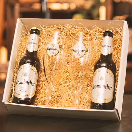 Geschenkbox mit zwei Krombacher Pils Bierflaschen und zwei passenden Biergläsern in Stroh.