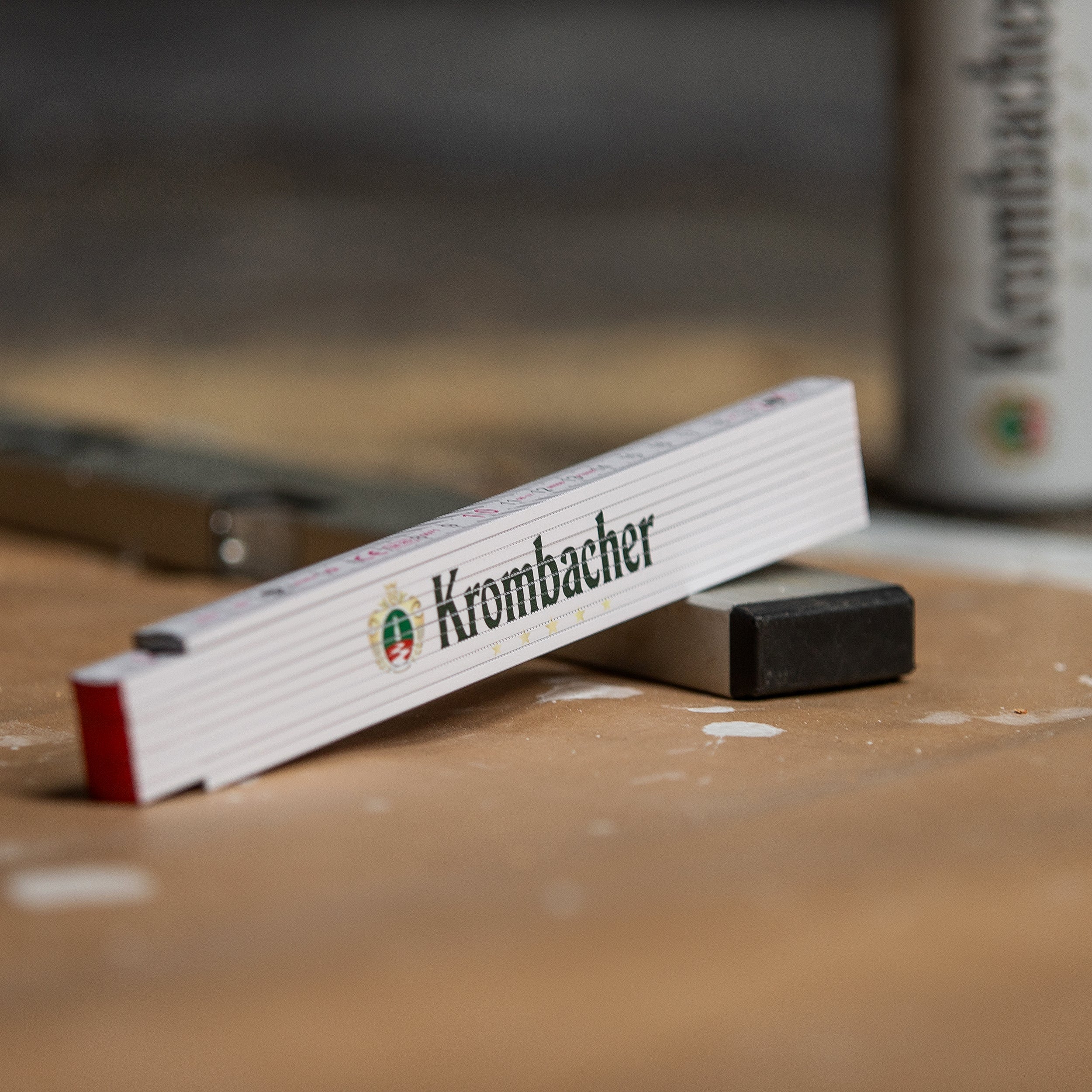 Zusammengeklappter weißer Zollstock mit grün-rotem Krombacher-Logo auf einer Werkbank
