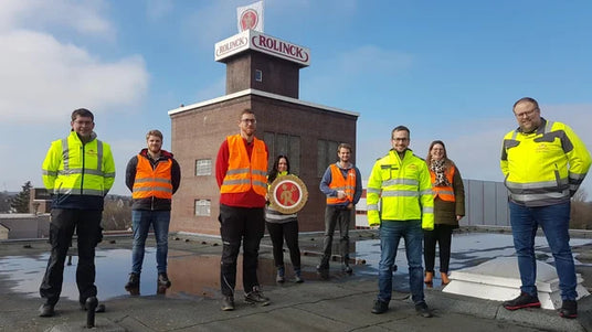 Rolinck Mitarbeitende in Warnwesten vor dem Rolinck-Gebäude mit Markenlogo auf dem Dach.