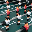 Nahaufnahme Tischfußballspieler in weißem und rotem Trikot auf grünem Spielfeld mit weißen Markierungen.