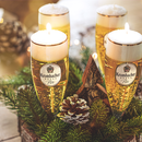 Vier Krombacher Pils Biergläser Kerzen, umgeben von Tannenzweigen und Zapfen als Adventskranz eingesetzt.