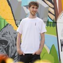 Ein Mann in einem weißen T-Shirt mit Krombacher Pils Flasche auf der Brust, vor einer bunten Wand.