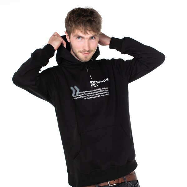 Person trägt schwarzen Hoodie mit Krombacher Pils Schriftzug und Text auf der Brust, Hände heben die Kapuze.