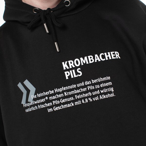Schwarzer Hoodie mit weißem Text 'Krombacher Pils' und Beschreibung des Biers mit 4,8 % Alkohol.