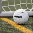 Weißer Fußball mit schwarzem Schriftzug 'DERBYSTAR' und Logos von Krombacher Spezi, liegt hinter der Torlinie auf grünem Rasen.