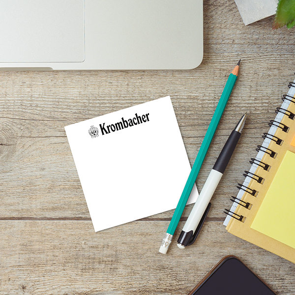 Notizzettel mit schwarzem Krombacher Logo auf einem Schreibtisch mit Laptop und Schreibutensilien.