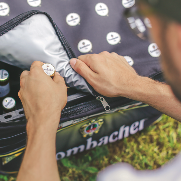 Person öffnet Reißverschluss einer Krombacher Bierkastenkühltasche und holt eine Flasche Krombacher Pils heraus.