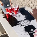 Person spielt Beerpong mit roten Bechern auf Krombacher-Matte auf weißem Tisch im Freien, Krombacher Pils Flasche daneben.
