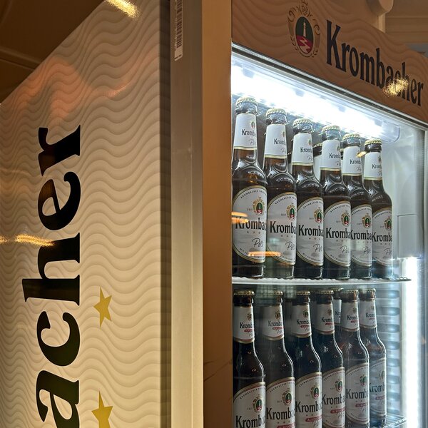 Kühlschrank mit Krombacher Bierflaschen, zwei Reihen mit Pils, beleuchtet.