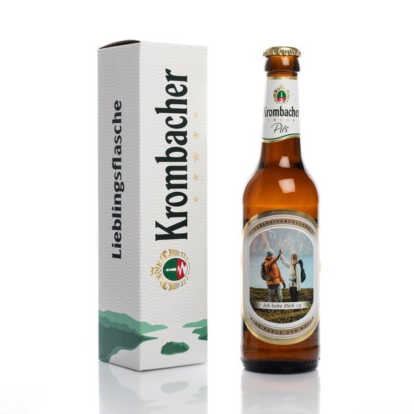 Krombacher Pils Bierflasche mit individuellem Etikett 'Ich liebe Dich <3' neben weißer Verpackung mit Schriftzug 'Lieblingsflasche Krombacher'.
