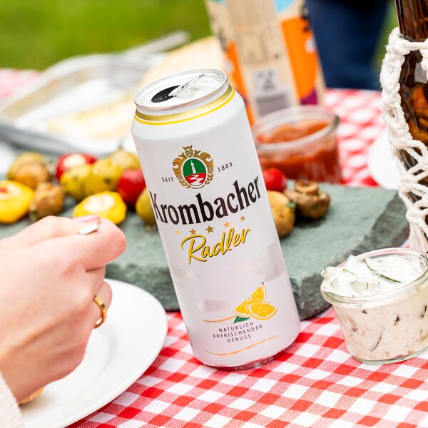 Krombacher Radler Bierdose auf einem Picknicktisch mit Snacks im Hintergrund