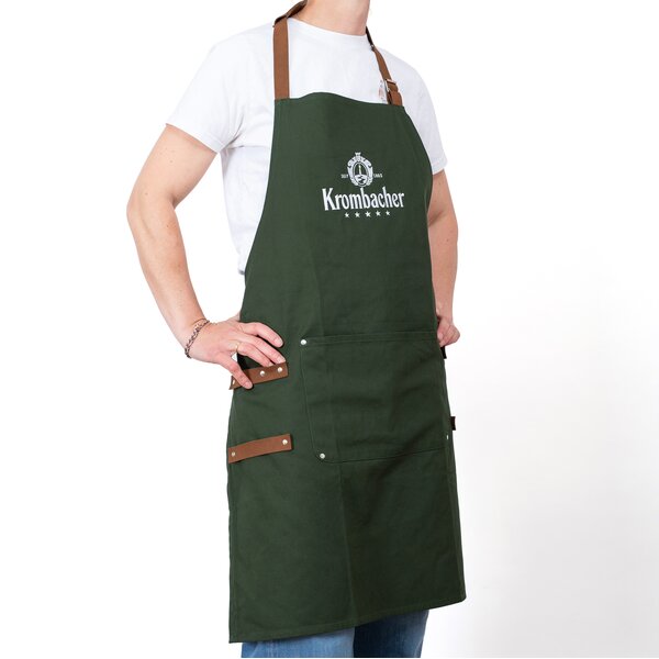 Person trägt grüne Krombacher Grillschürze mit braunen Trägern und Logo auf der Brust, drunter weißes T-Shirt.