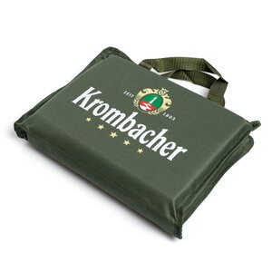 Grünes, quadratisches Stadionsitzkissen mit Tragegriff und weißem Schriftzug 'Krombacher' sowie Logo.