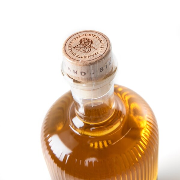 5553_krombachershop_Bierbrand_Der_Traditionelle_Produkt_002 Flasche mit goldenem Bierbrand, Holzverschluss mit Prägung und Text 'PREMIERTE QUALITÄT' und Blätter-Motiv.