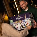 Personen mit Krombacher Adventskalender. Zwei Personen halten gemeinsam einen Krombacher Adventskalender mit winterlicher Illustration und nummerierten Türchen.