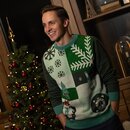 Mann trägt grünen Weihnachtspullover mit Schneeflocken, Tannenbaum und Rentier, steht vor geschmücktem Weihnachtsbaum.