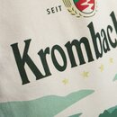 Nahaufnahme eines hellen Jutebeutels mit dem schwarzen Schriftzug 'Krombacher' und dem Teil eines Logos mit roten und goldenen Elementen.