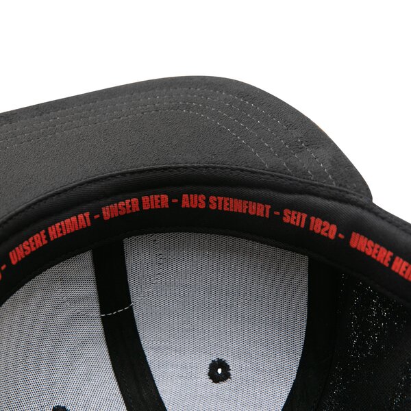 Innenseite einer schwarzen Kappe mit rotem Text am Schweißband: 'UNSERE HEIMAT - UNSER BIER - AUS STEINFURT - SEIT 1820'.
