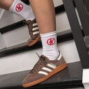 Beine mit weißen Tennissocken, die ein rotes rundes Logo zeigen, und braune Adidas-Sneaker mit weißen Streifen und brauner Sohle auf schwarzen Stufen.