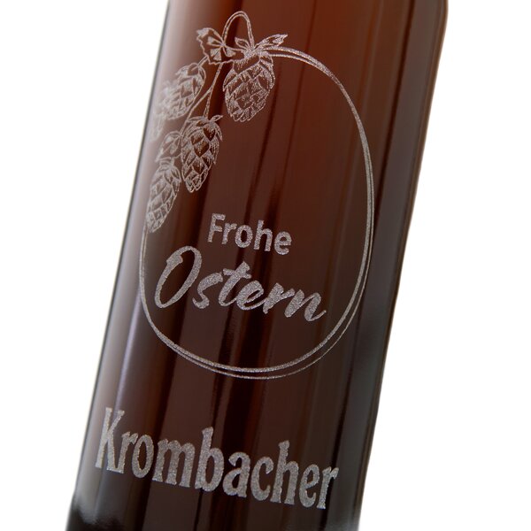 Braune Flasche mit der gravierter Aufschrift 'Frohe Ostern' und 'Krombacher' sowie einer Illustration von Hopfenzapfen und einem Osterei
