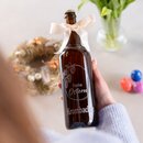 Hand hält eine braune Glasflasche mit eingraviertem Schriftzug 'Frohe Ostern' und Krombacher Logo einer hellen Schleife am Flaschenhals.