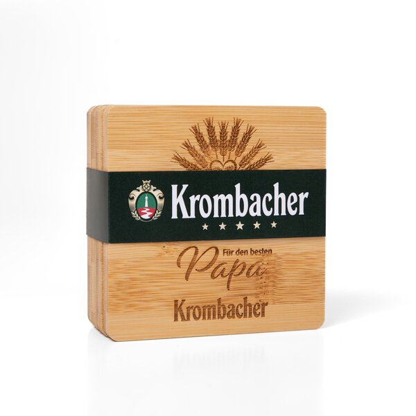Holzuntersetzer mit eingraviertem Schriftzug "Für den besten Papa" und dem Krombacher-Logo auf dunkel grünem Band.