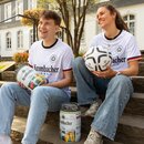 Zwei Personen sitzen auf einer Treppe, beide tragen weiße Krombacher-Trikots, eine Person hält ein Krombacher-Fass, die andere einen Fußball mit Krombacher-Logo.