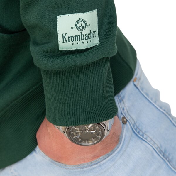 Nahaufnahme eines dunkelgrünen Krombacher-Hoodies mit Logo auf dem Ärmel